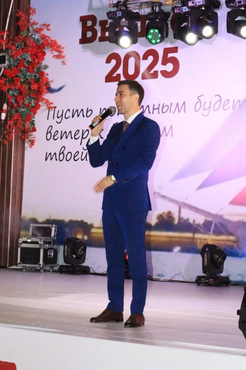 Ведущий на сцене выпускного вечера с надписью «Выпускной 2025»